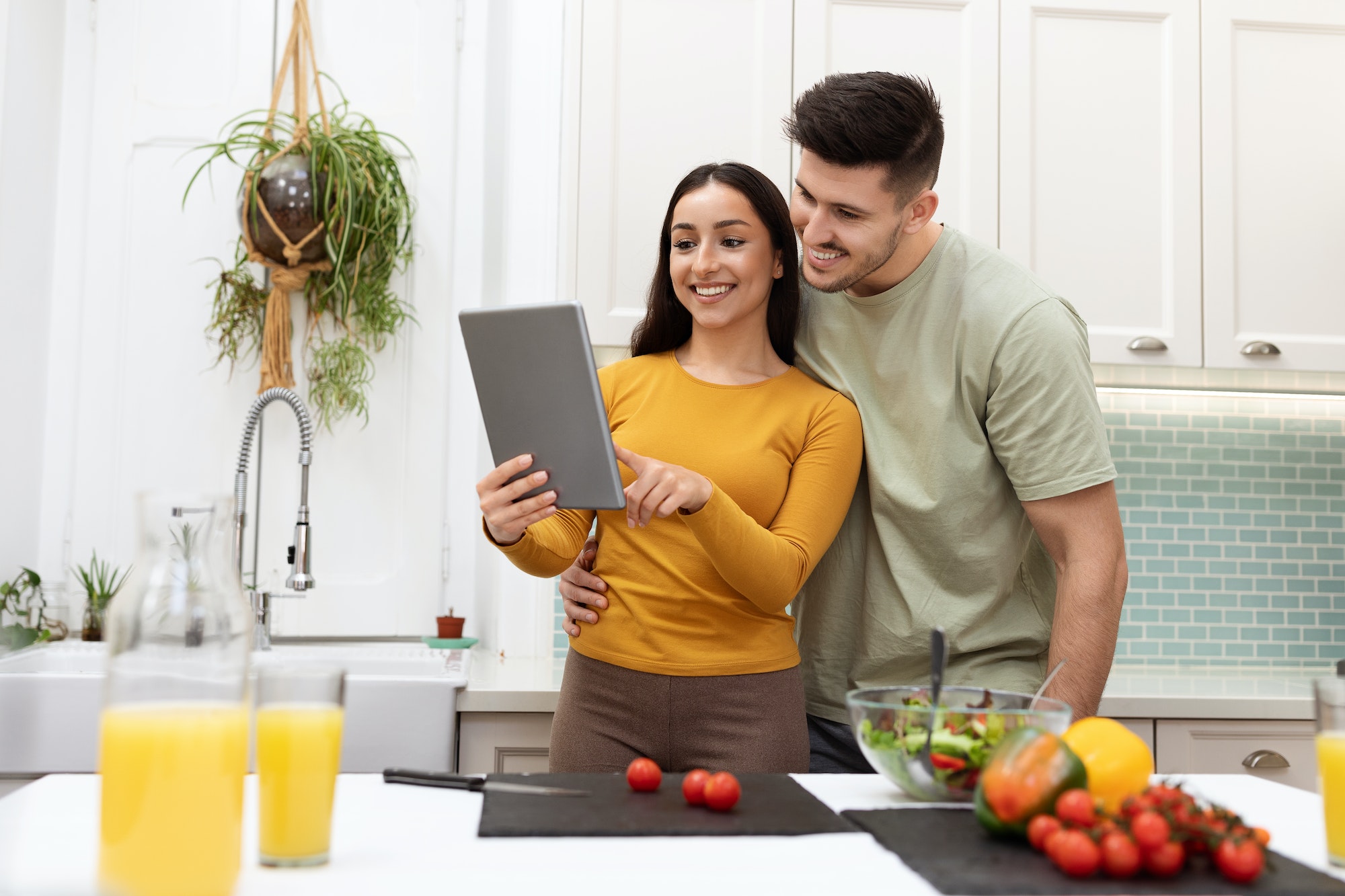 Cheerful hispanic couple looking for recipe on Internet, using pad